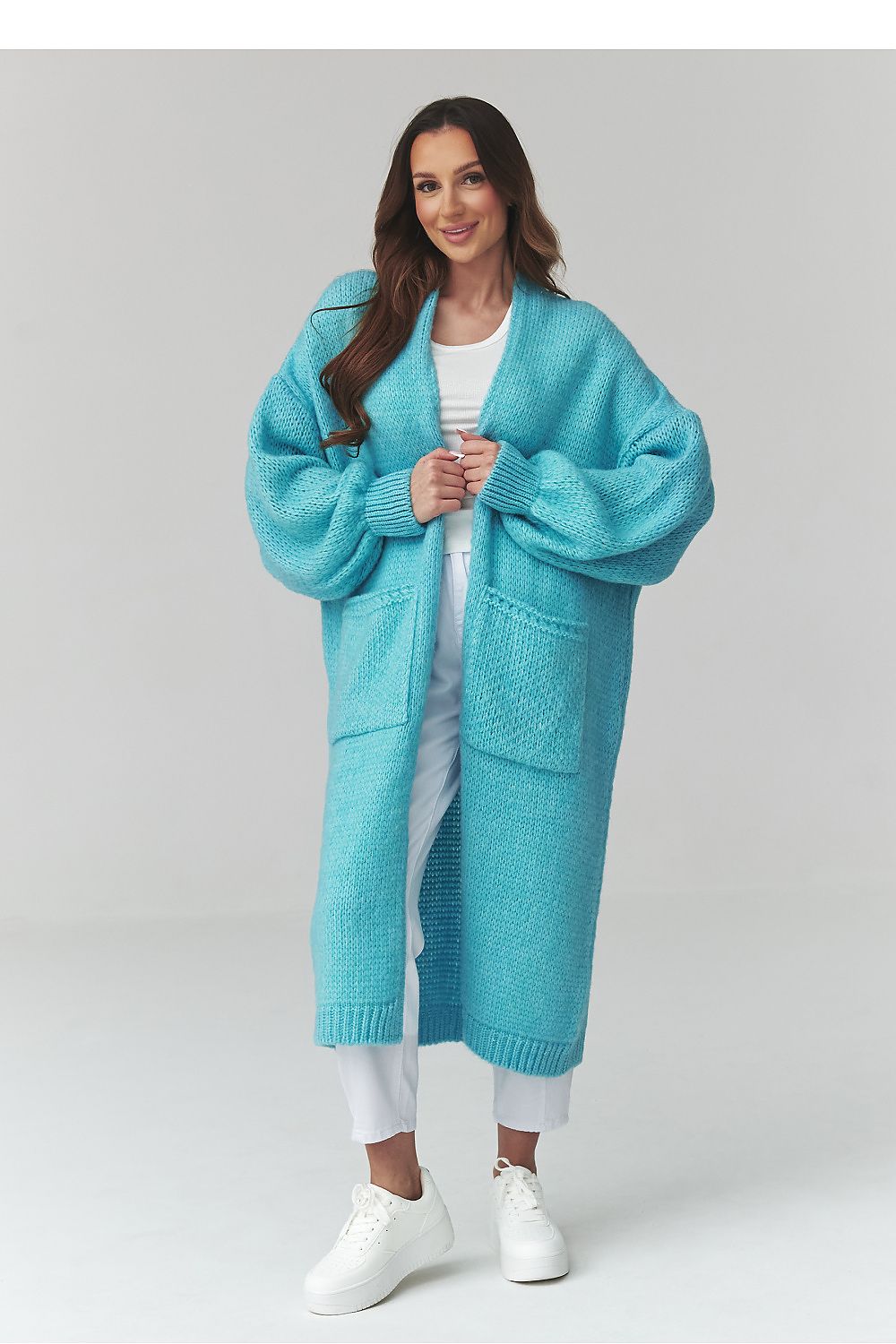 Woman wearing a long turquoise cardigan on a white background