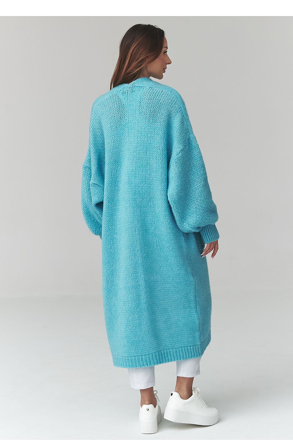 Person wearing a long turquoise cardigan on a plain background