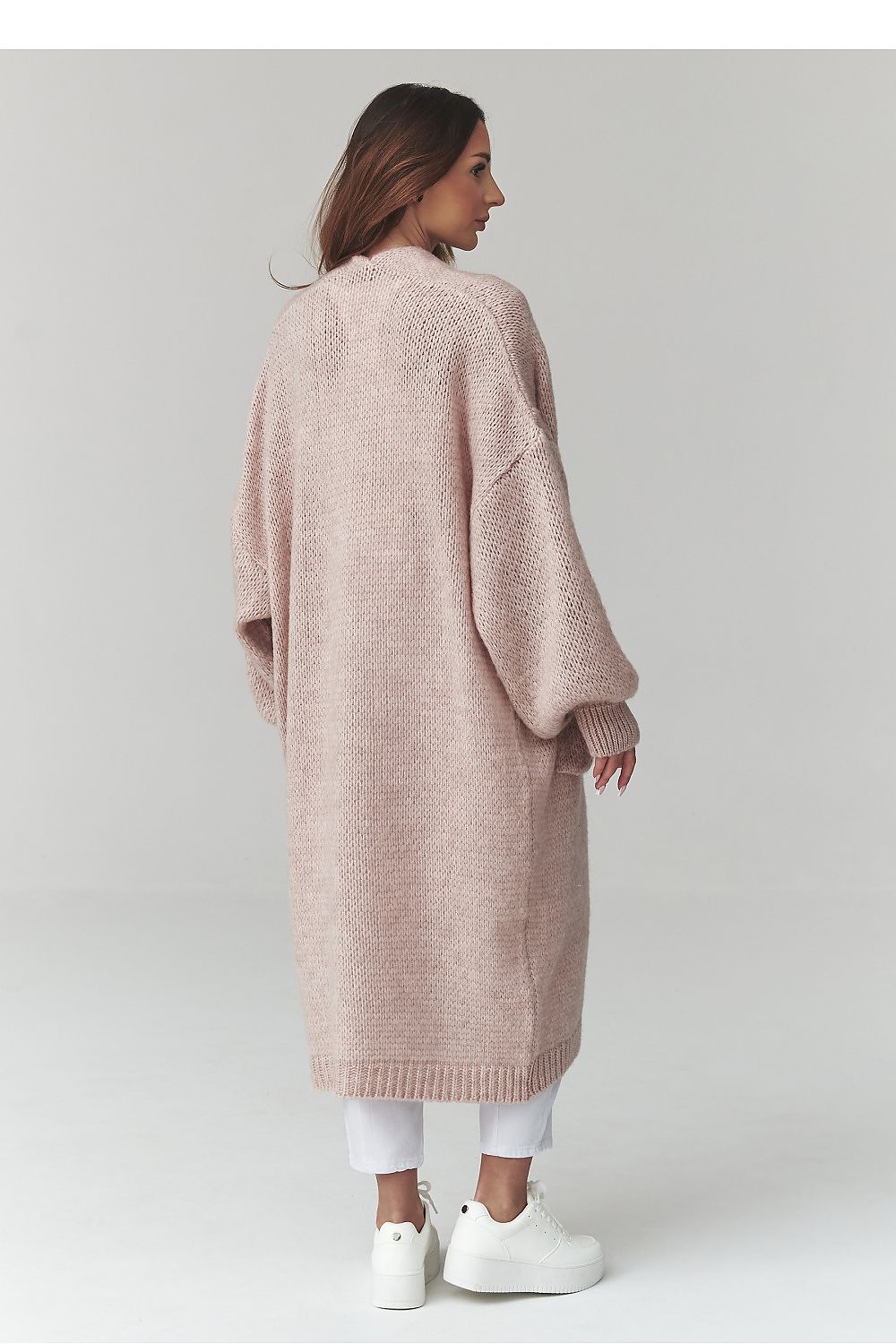 Woman wearing a long beige cardigan on a plain background