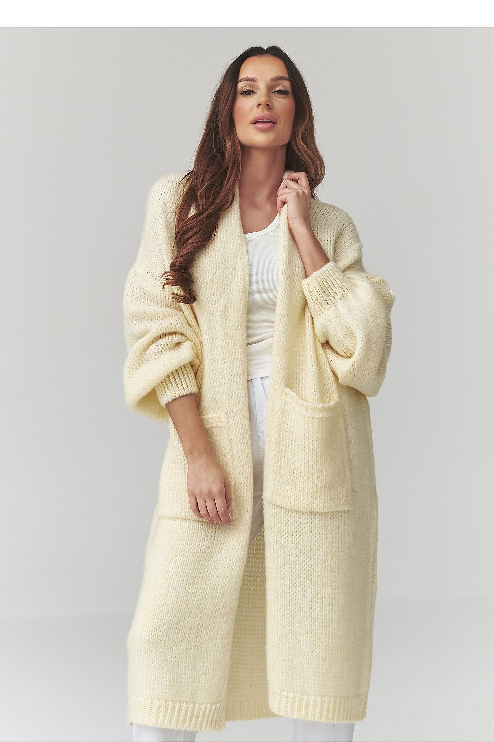 Woman wearing a long cream cardigan on a light gray background
