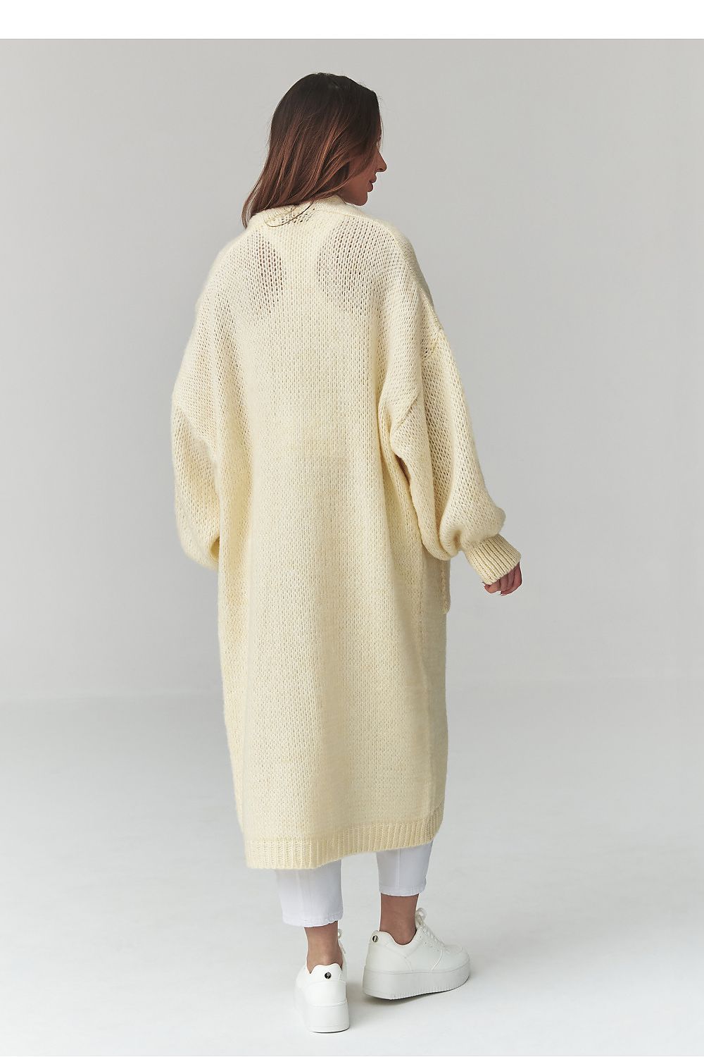 Woman wearing a long light yellow cardigan on a white background