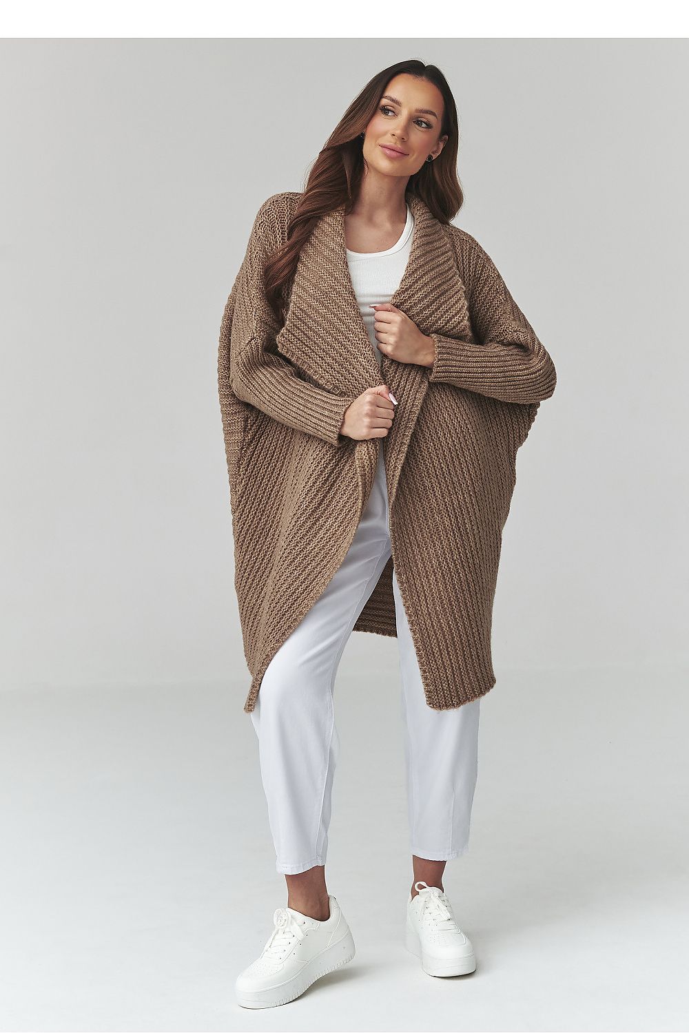 Woman wearing a brown knitted cardigan over a white outfit on a light gray background