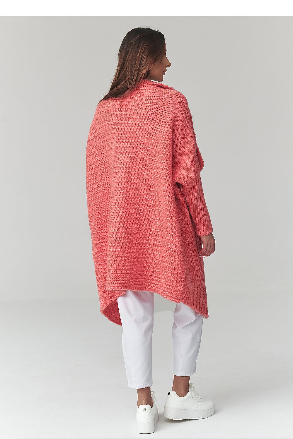 Woman wearing a pink poncho over a white outfit on a light gray background