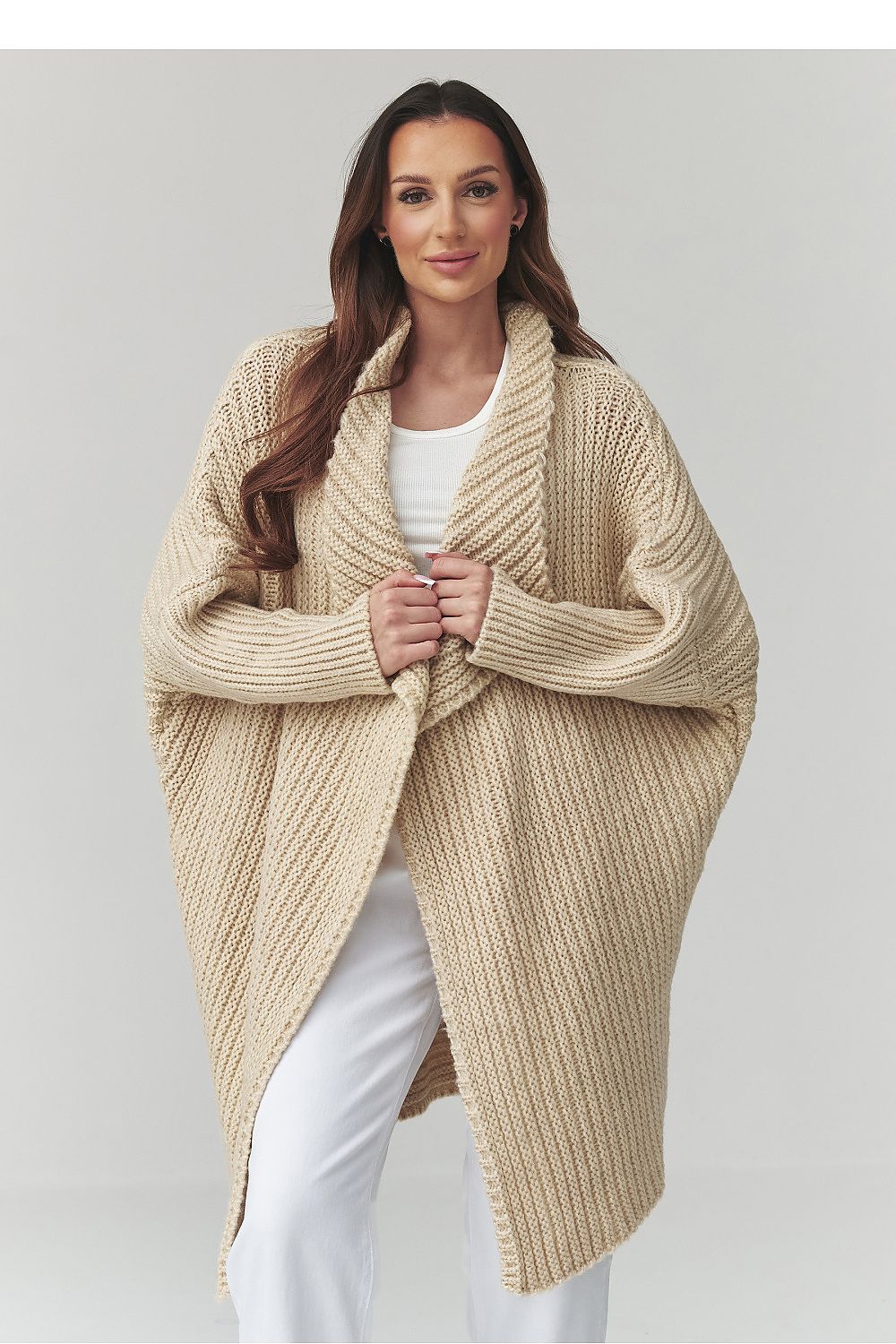 Woman wearing a beige knitted poncho against a plain background