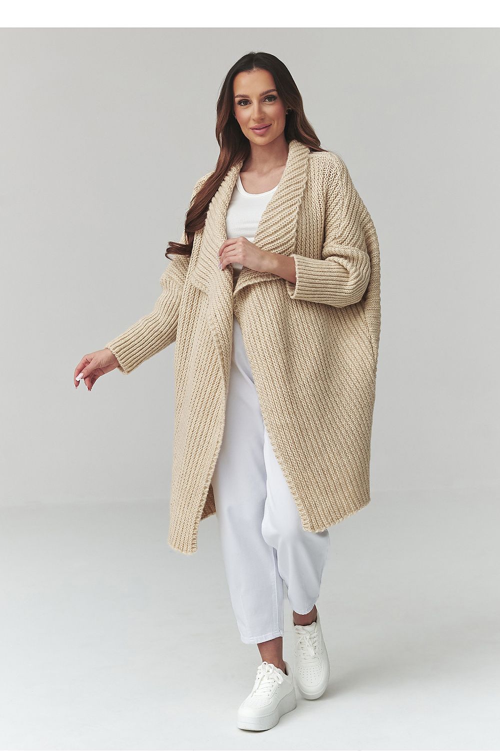 Woman wearing a beige cardigan over a white outfit on a plain background
