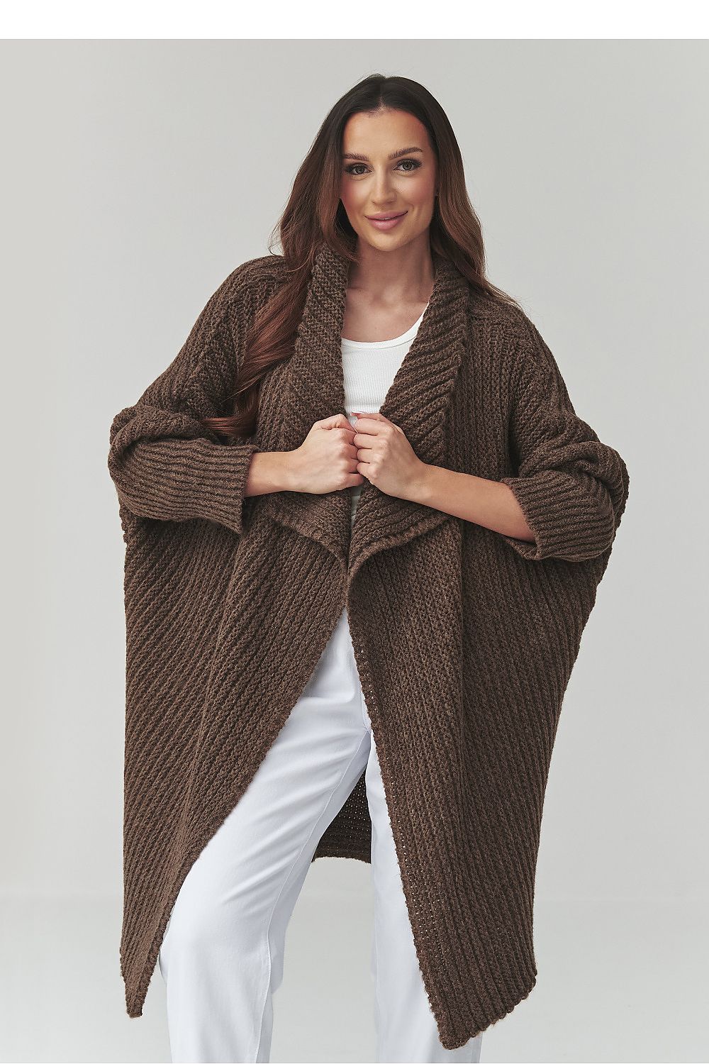 Woman wearing a brown knitted poncho over a white outfit on a light gray background