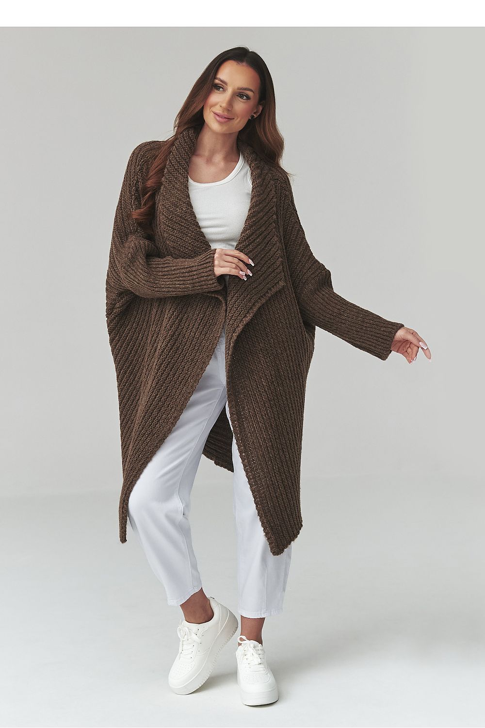 Woman wearing a brown knitted coat over a white outfit on a plain background