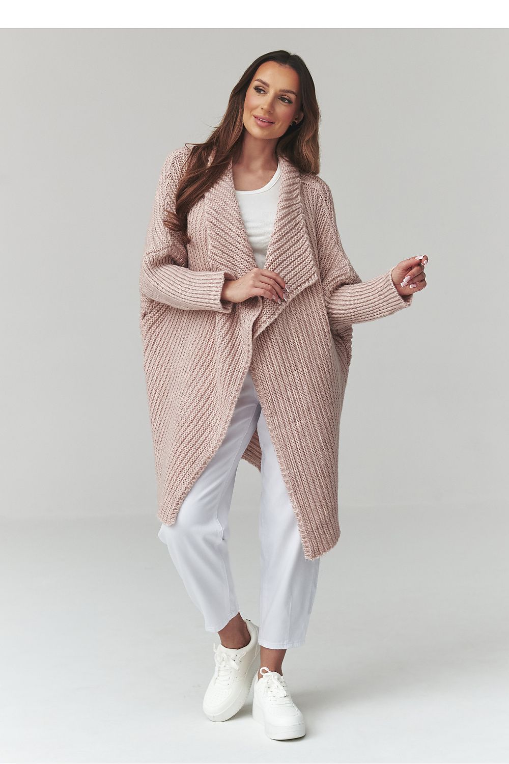 Woman wearing a pink knitted cardigan over a white outfit on a light gray background