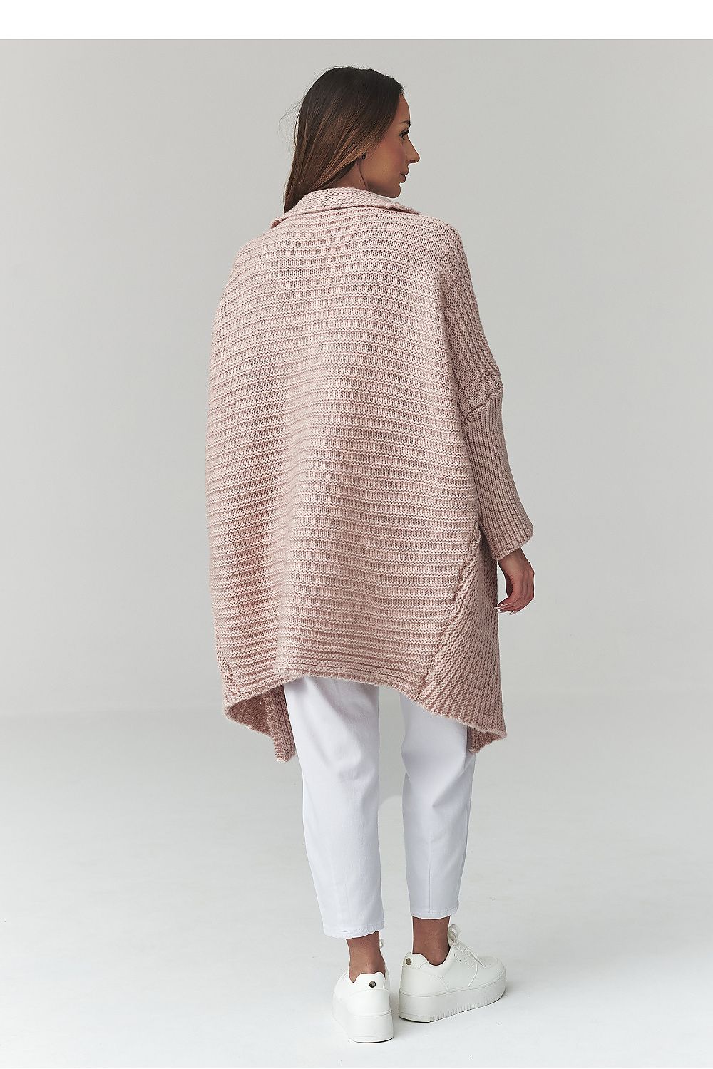 Woman wearing a pink striped sweater over a white top and pants on a light gray background