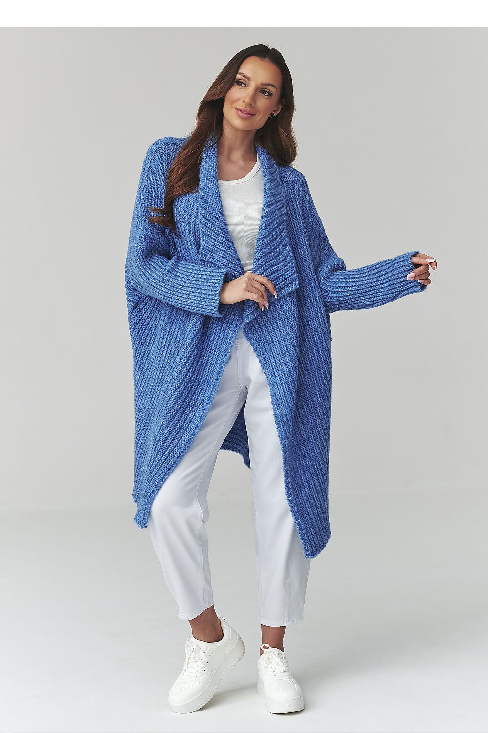 Woman wearing a blue knitted cardigan over a white outfit on a light gray background