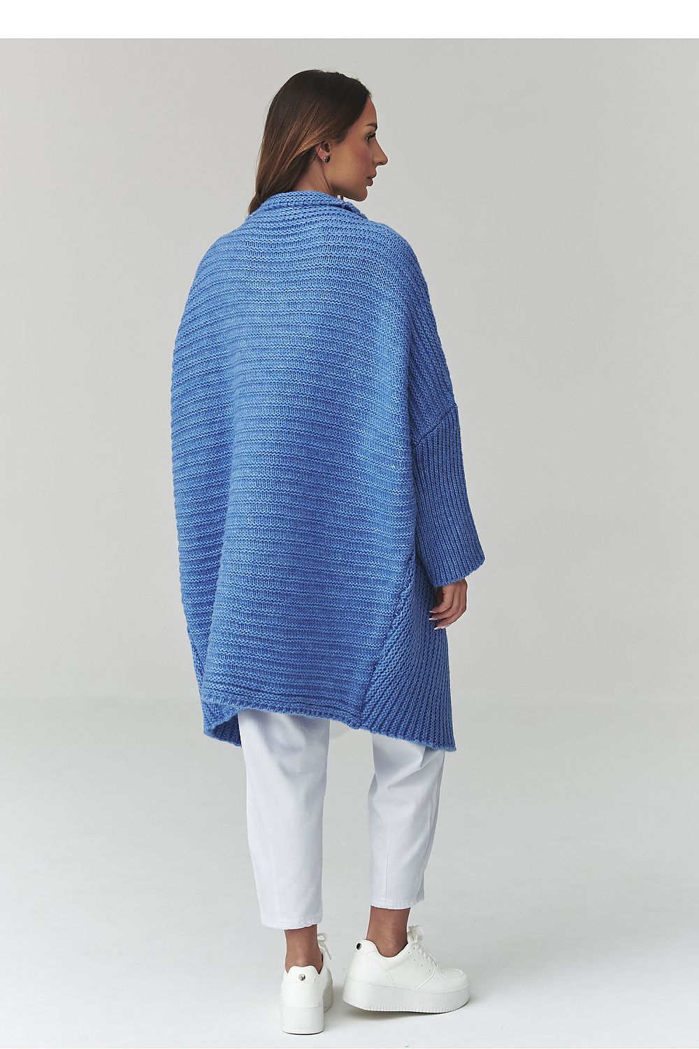 Woman wearing a blue knitted poncho on a plain background