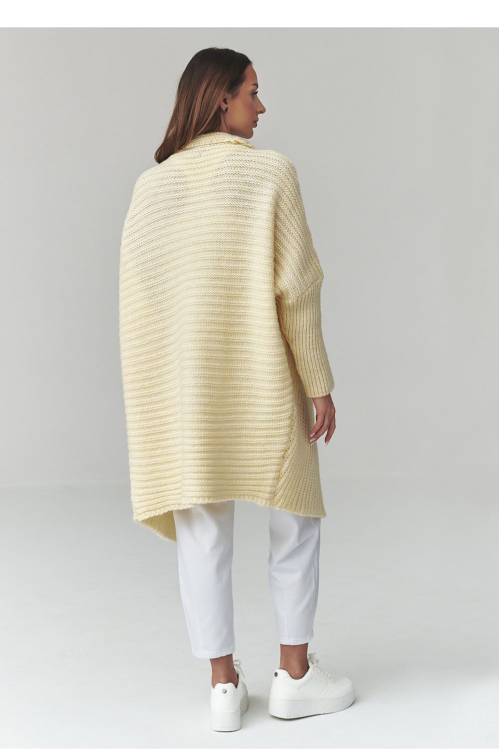 Woman wearing a light yellow ribbed sweater and white pants on a plain background