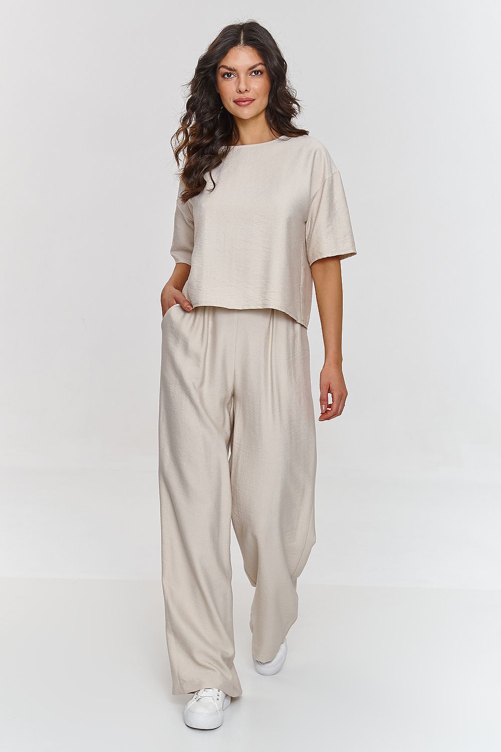 Woman wearing a beige outfit with wide-leg pants on a white background
