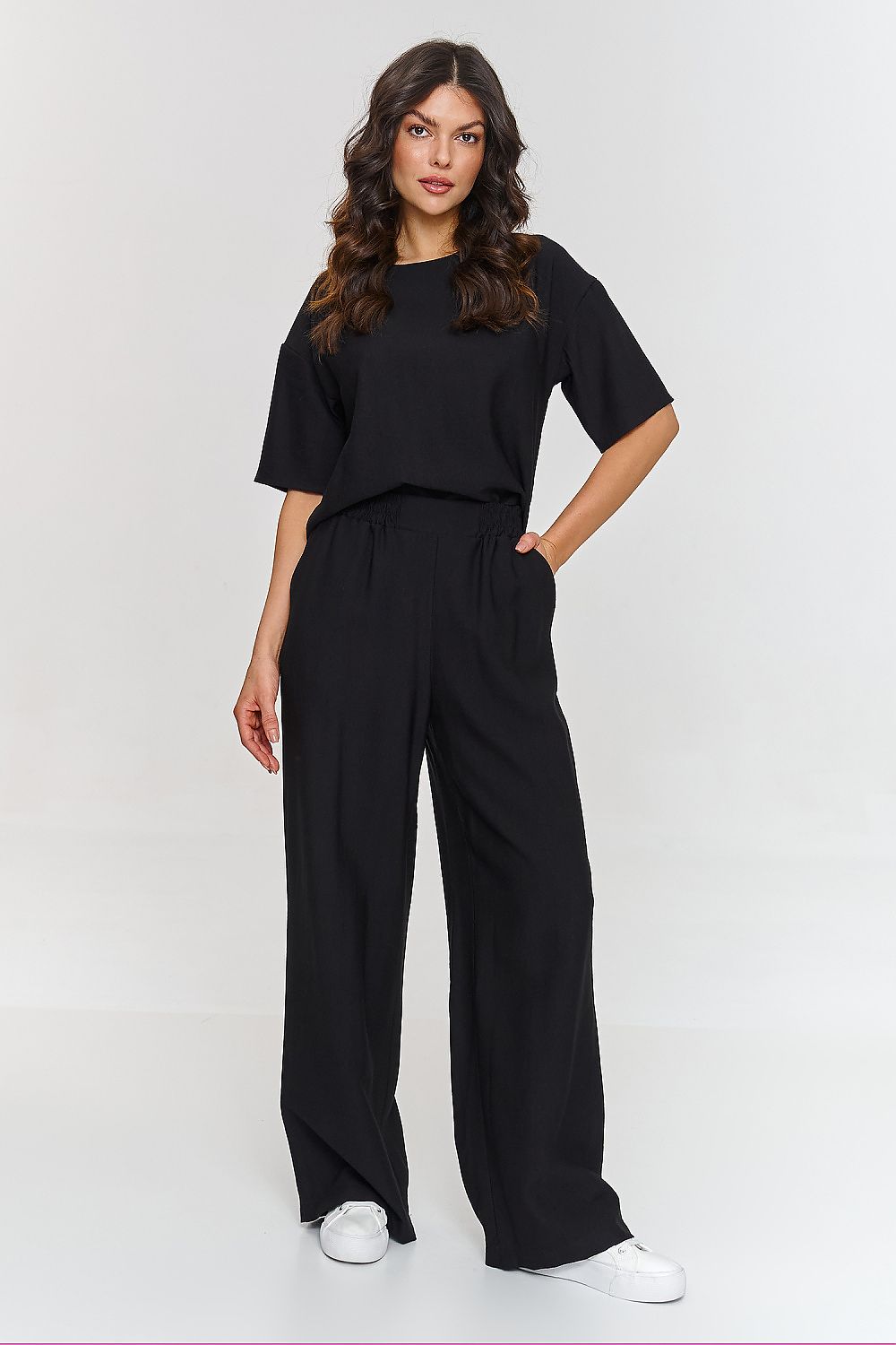 Woman wearing a black outfit with wide-leg pants on a white background