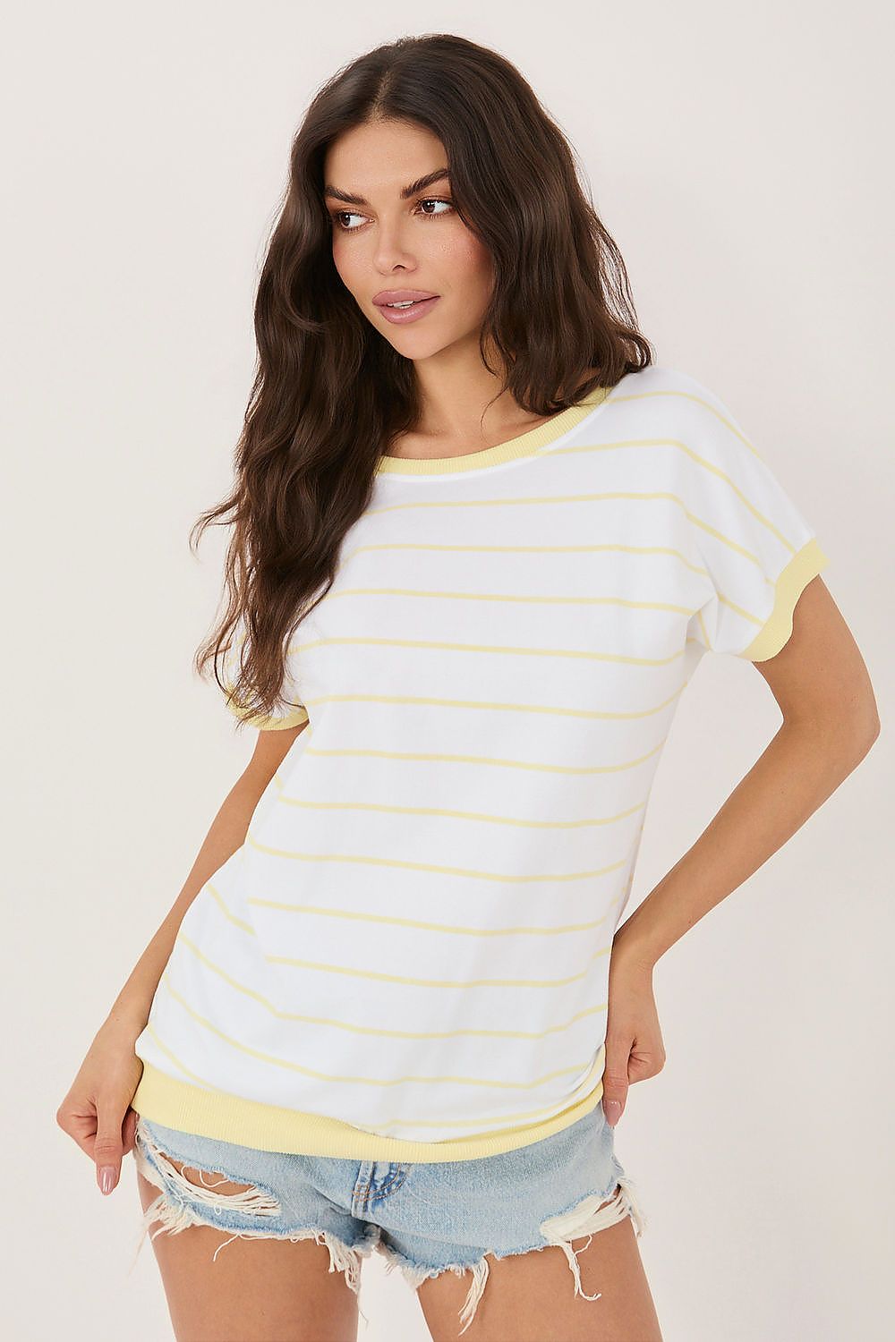 Woman wearing a white and yellow striped shirt with denim shorts on a plain background