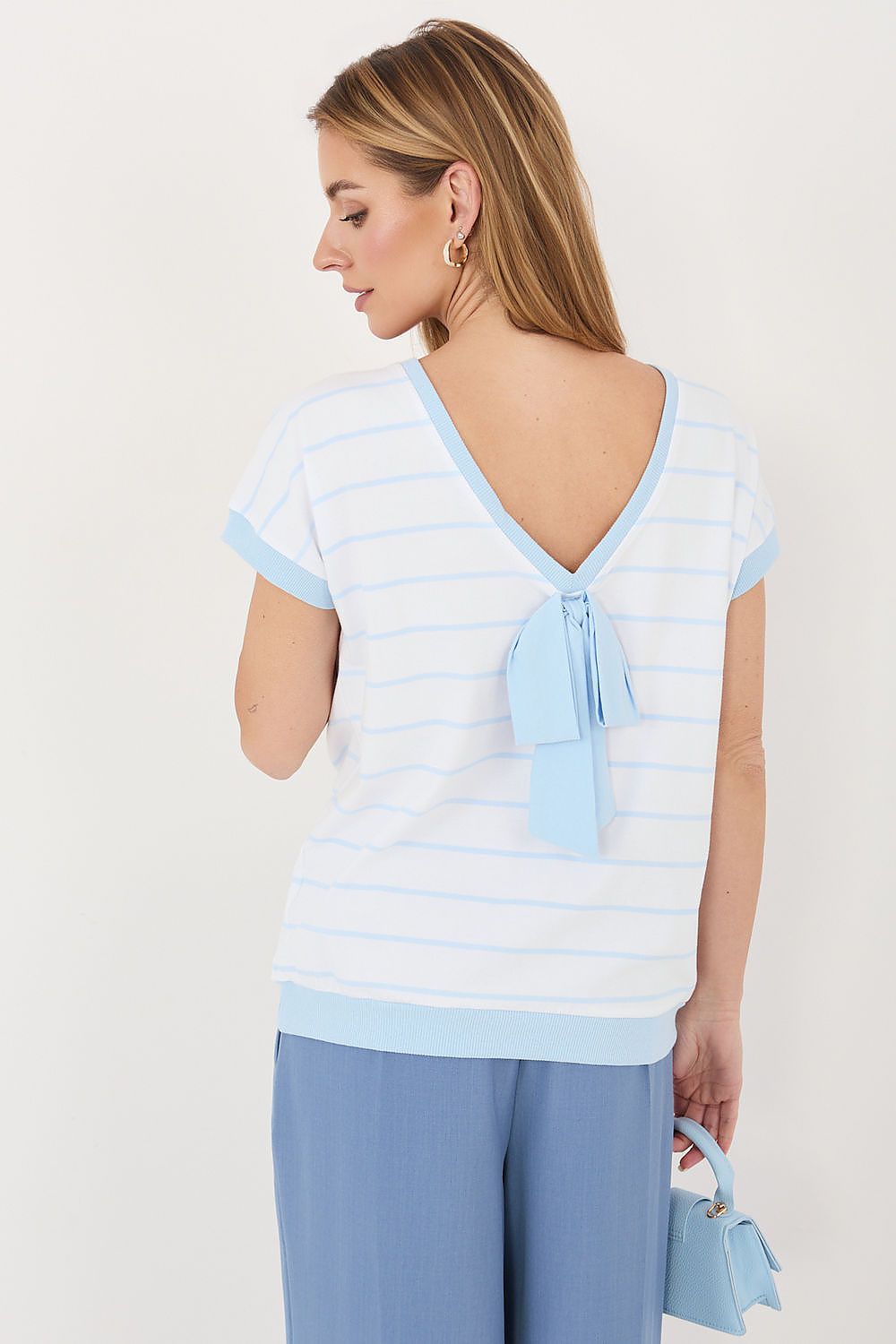 Woman wearing a light blue and white striped top with a bow detail on a plain background