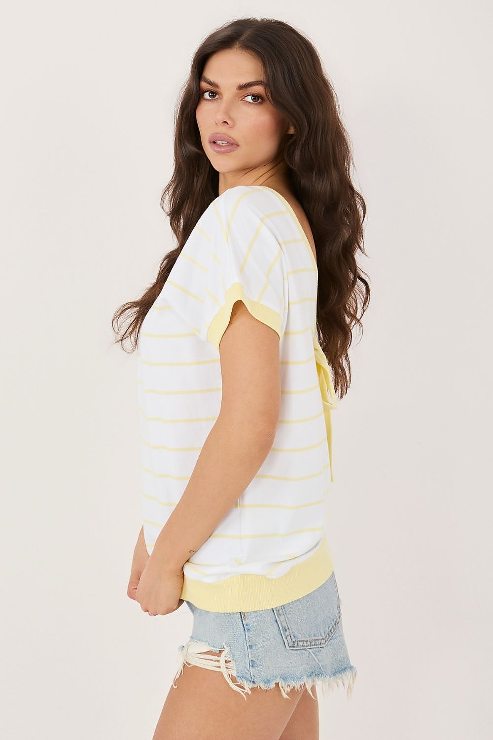 Woman wearing a white and yellow striped shirt with denim shorts on a plain background