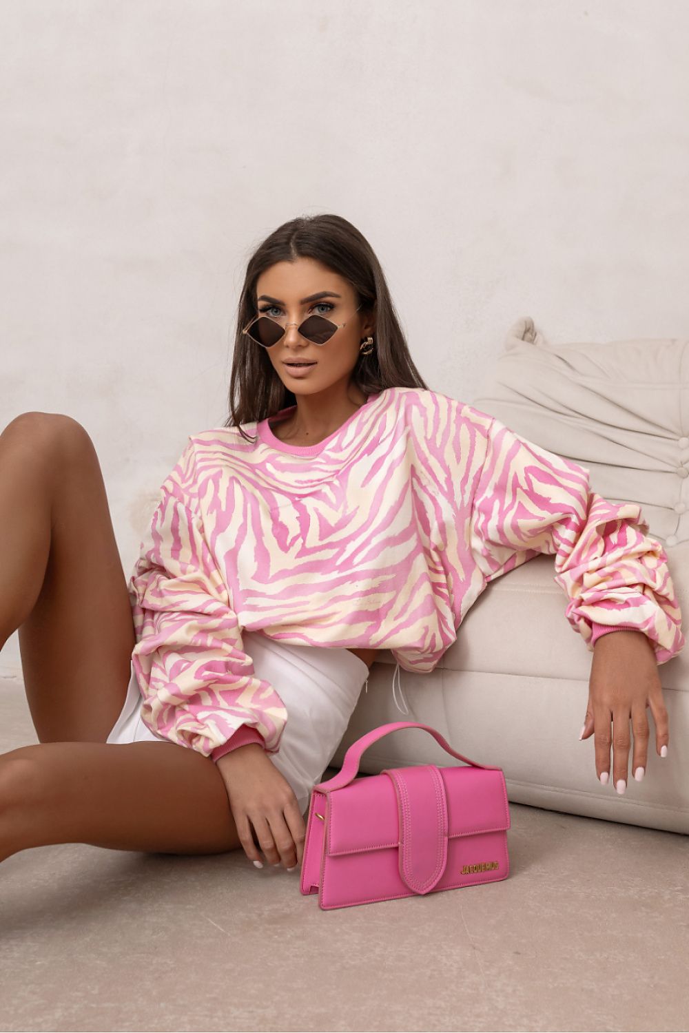 Woman in a pink and white tie-dye outfit with a pink handbag on a light background