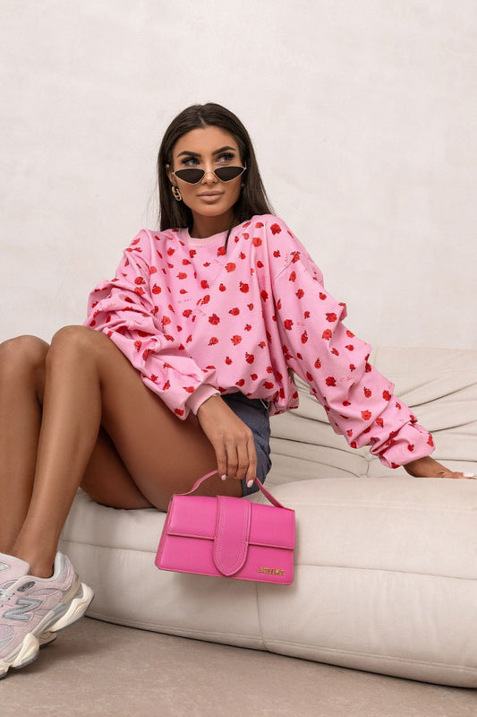 Woman in pink heart-patterned sweater holding a pink handbag on a white couch.