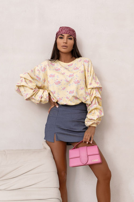 Woman wearing a floral blouse and denim skirt, holding a pink handbag against a plain background