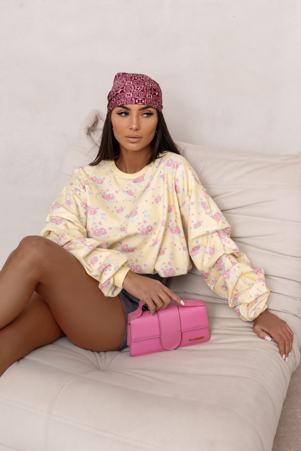 Woman sitting on a couch wearing a floral headscarf and holding a pink clutch.