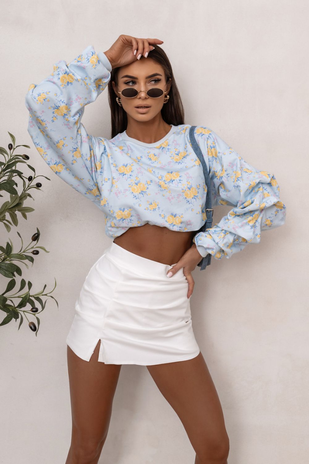 Woman wearing a light blue floral blouse and white skirt against a plain background