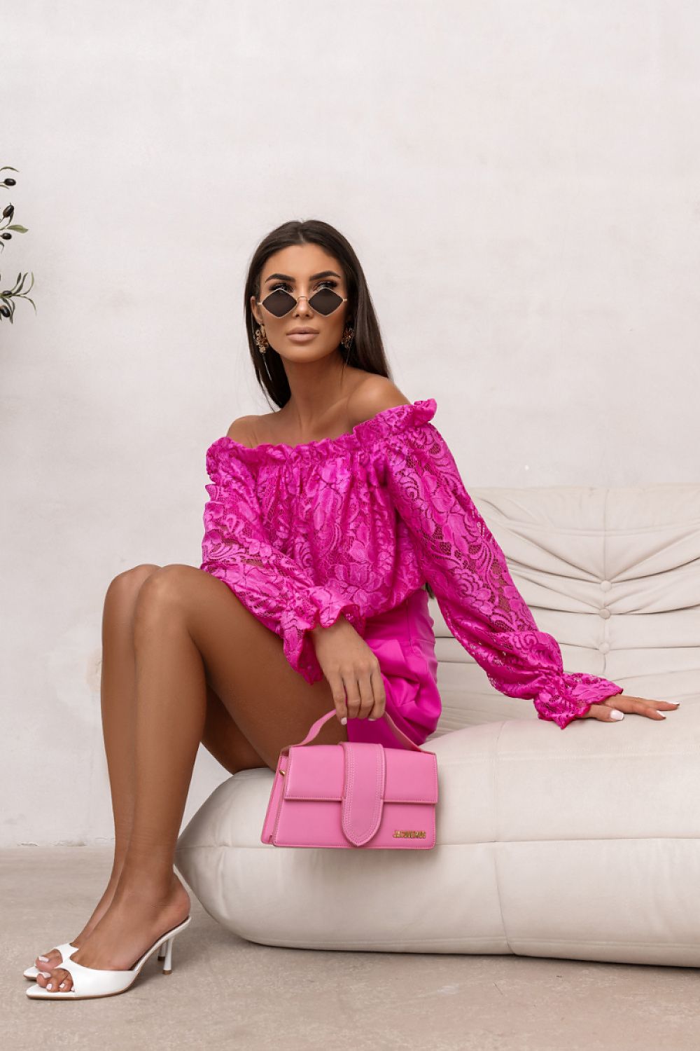 Woman in a bright pink outfit with a matching handbag sitting on a beige couch.