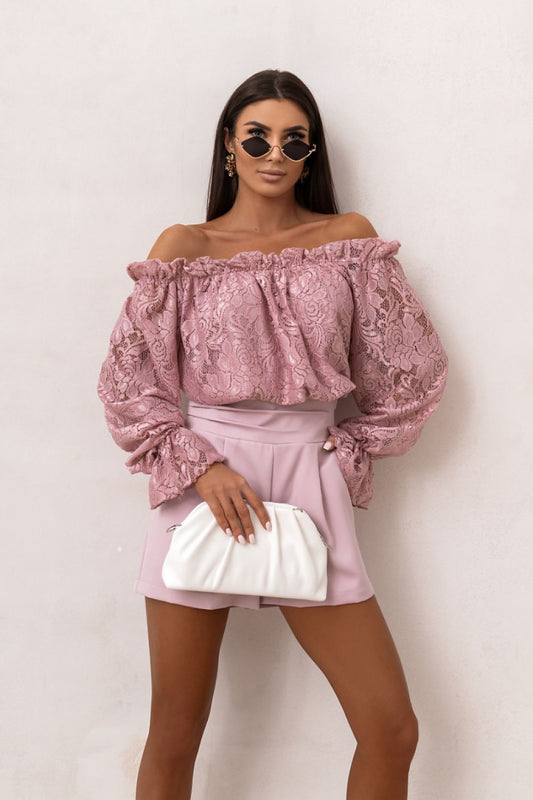 Woman wearing a pink lace top and skirt with a white clutch against a light background