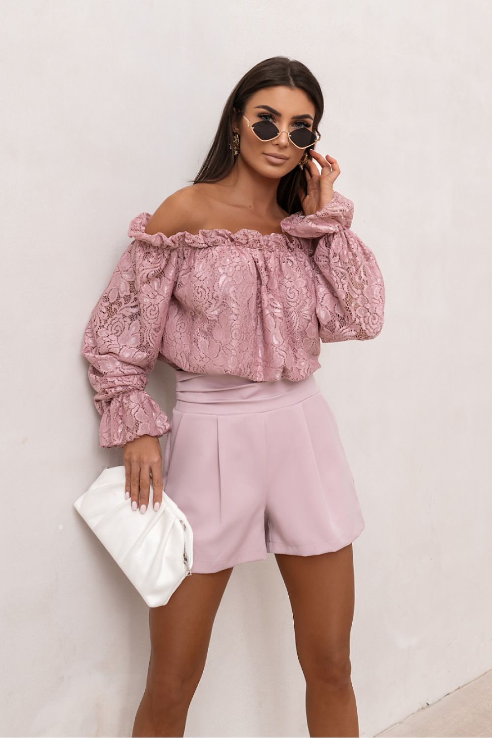 Woman wearing a pink floral blouse and shorts against a white background