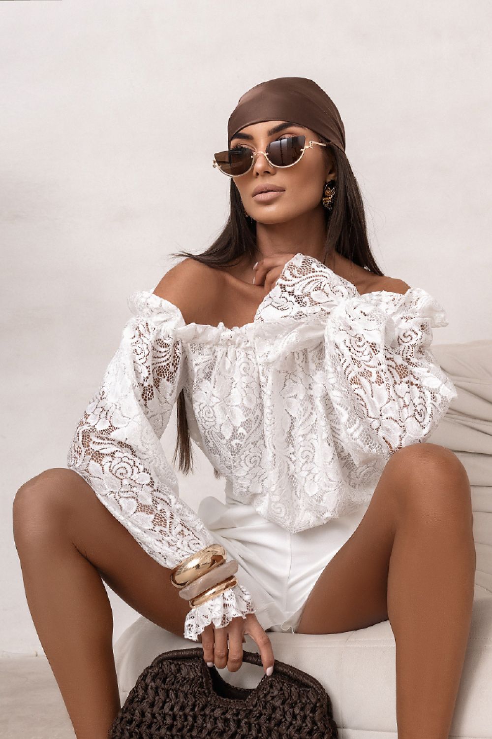 Woman wearing a white lace top and sunglasses, sitting on a couch.