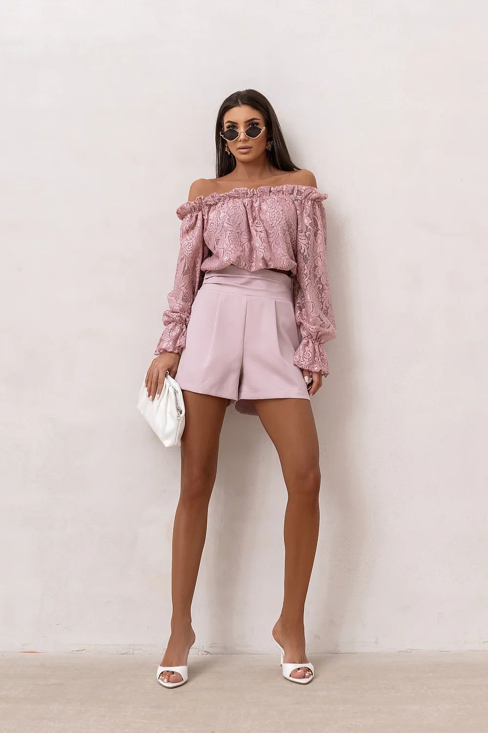 Woman wearing a pink off-shoulder top and shorts against a white background