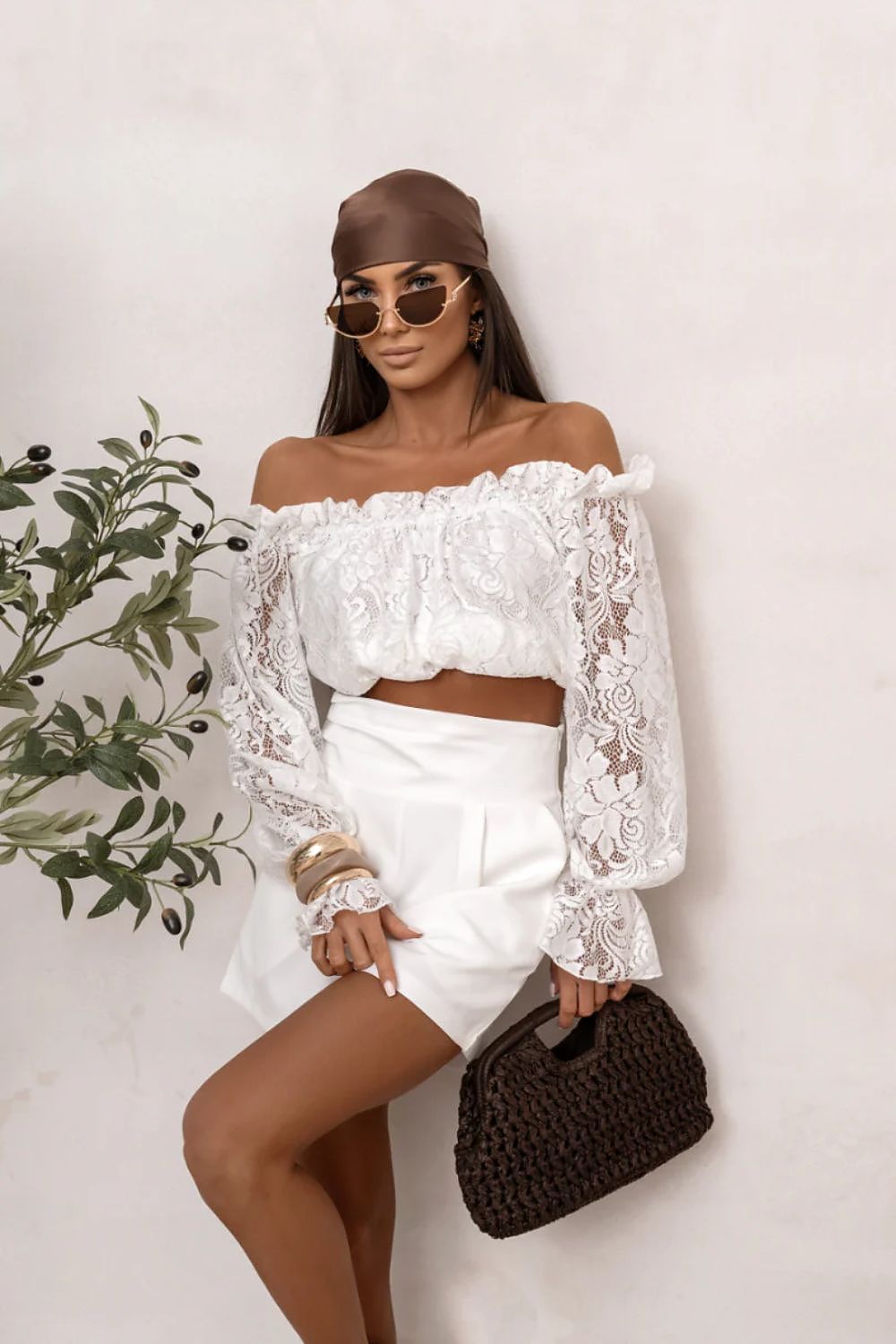 Woman wearing a white lace top and shorts with a black handbag against a white background