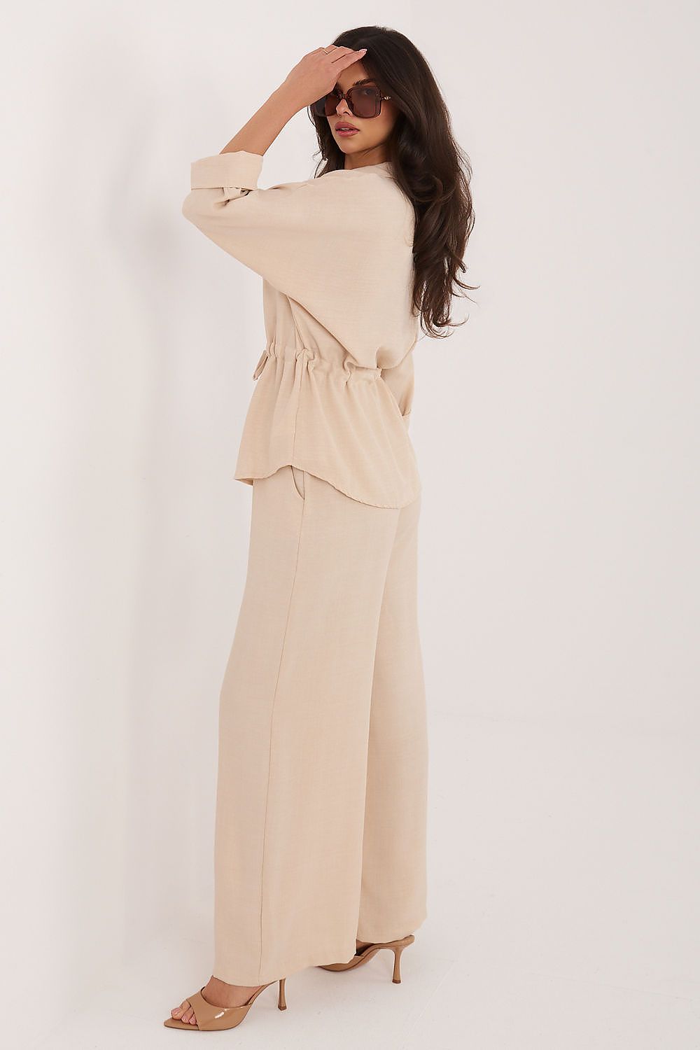 Woman wearing a beige outfit with sunglasses on a white background