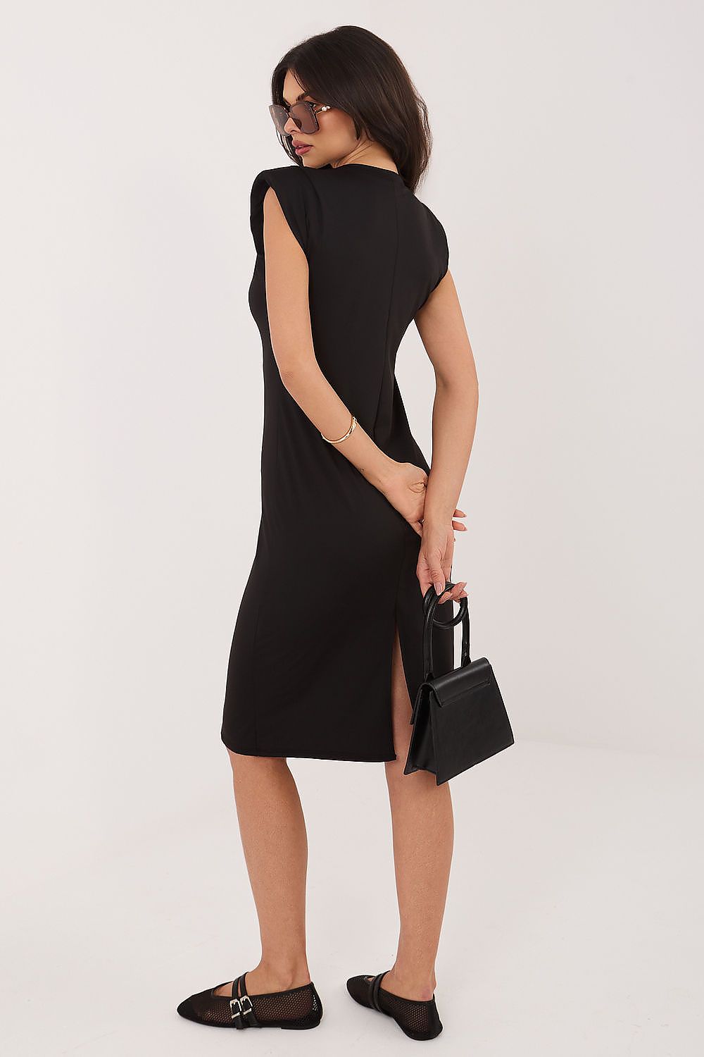 Woman wearing a black sleeveless dress holding a black handbag on a white background
