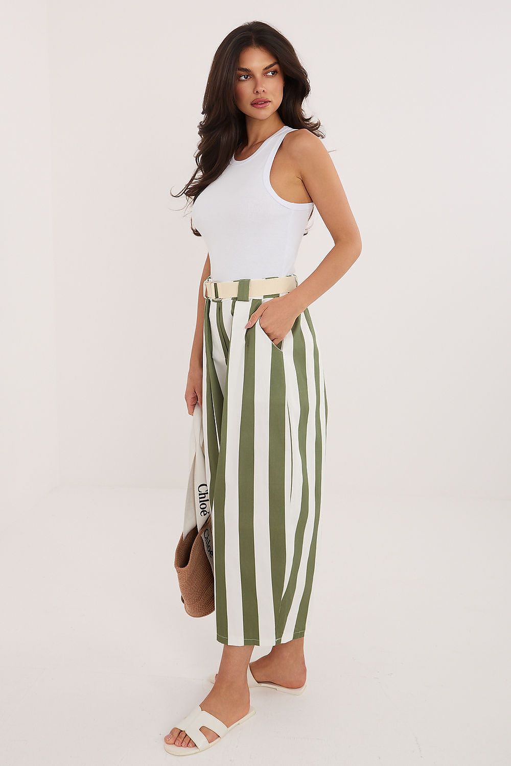 Woman wearing a white sleeveless top and green and white striped pants on a white background