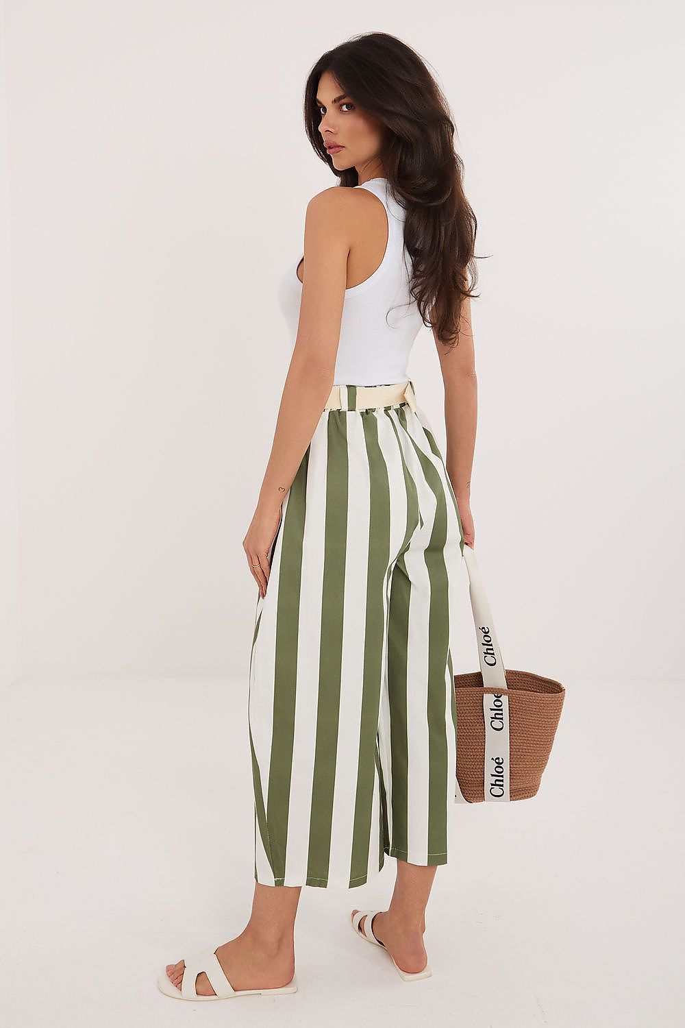 Woman wearing green and white striped pants with a white top, holding a brown bag with visible branding.