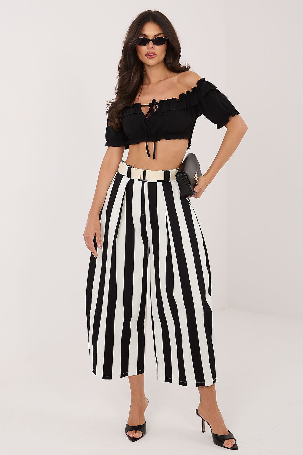Woman wearing a black off-shoulder top and black and white striped pants on a white background