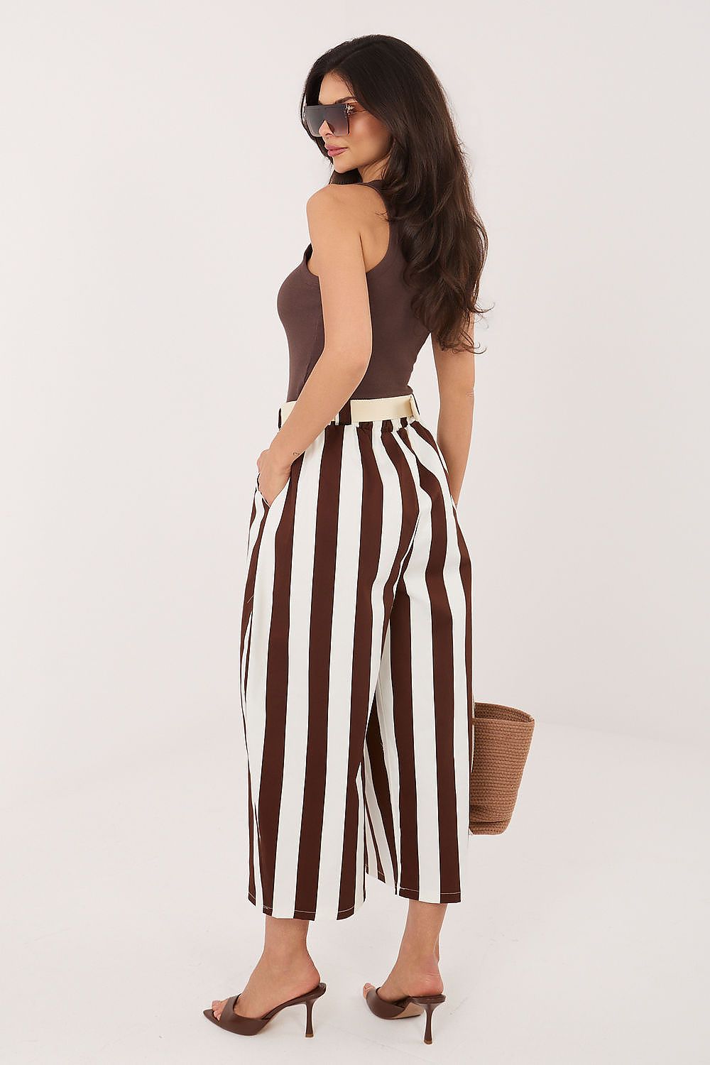 Woman wearing a brown top and white striped pants on a white background