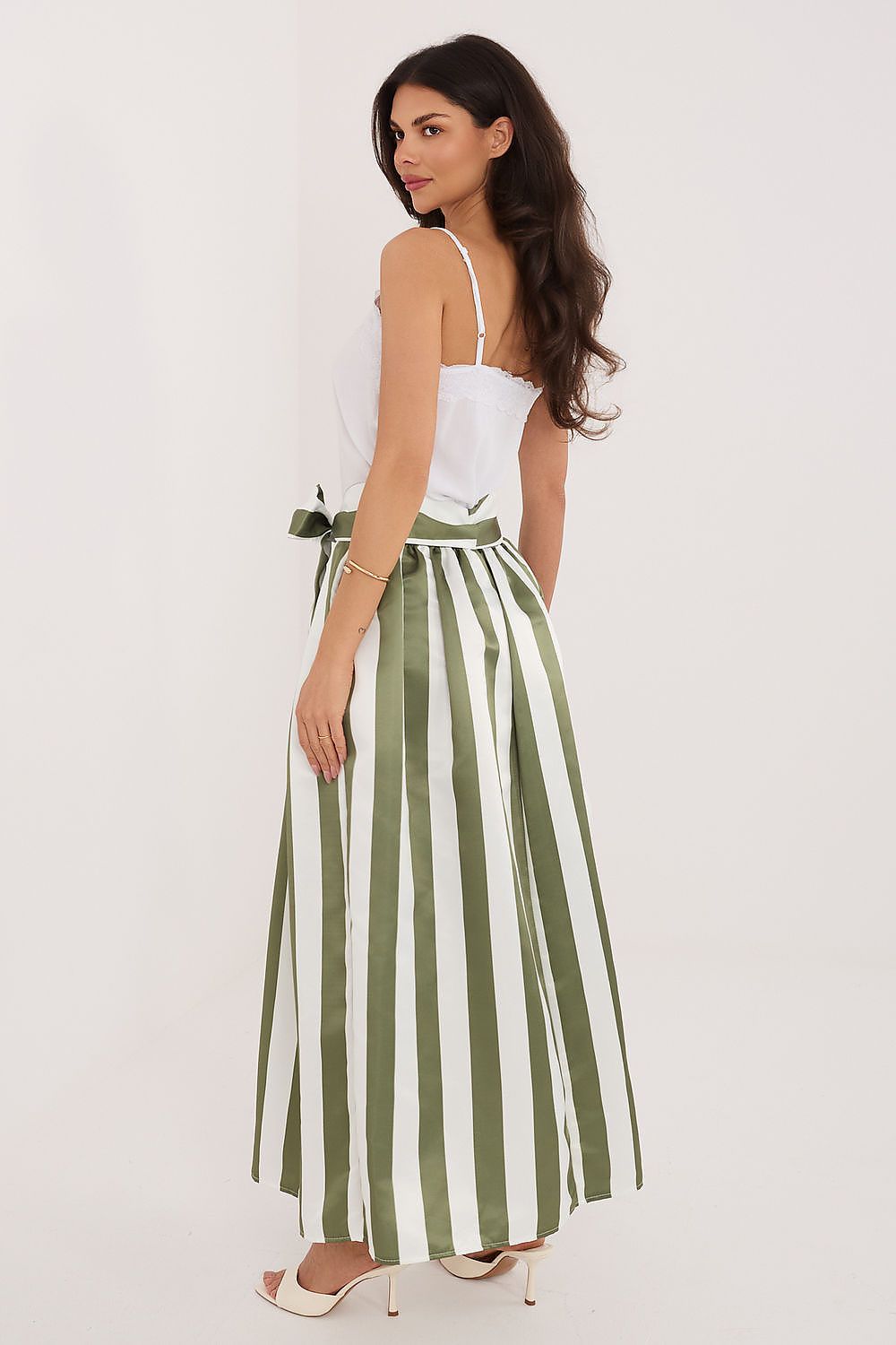 Woman wearing a white top and green and white striped skirt on a light background