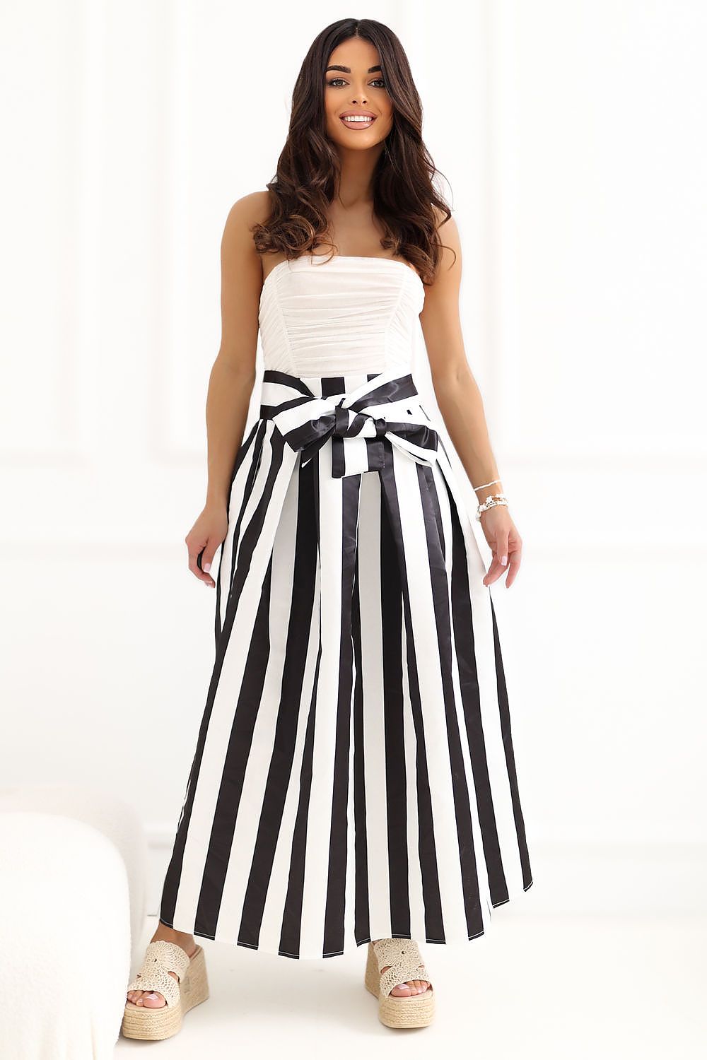 Woman wearing a strapless dress with a black and white striped skirt on a white background