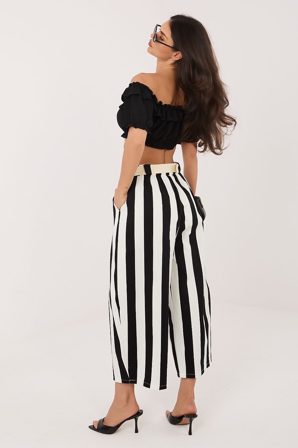 Woman wearing a black off-shoulder top and black and white striped pants on a white background