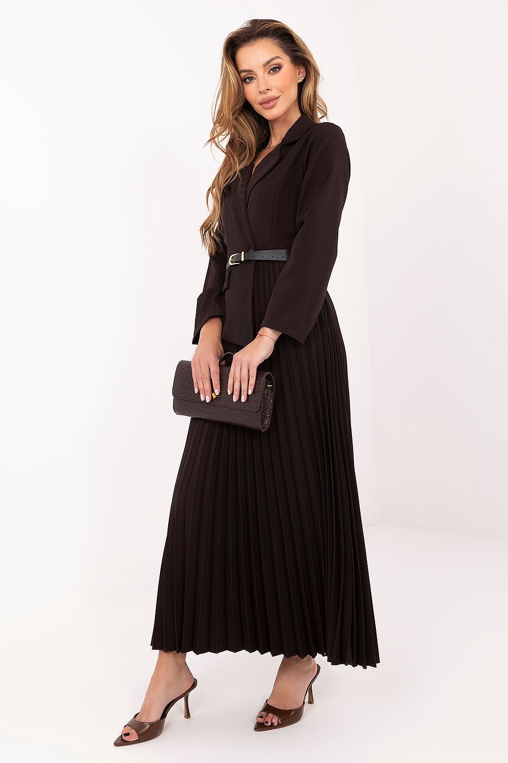 Woman wearing a black pleated dress holding a clutch against a white background