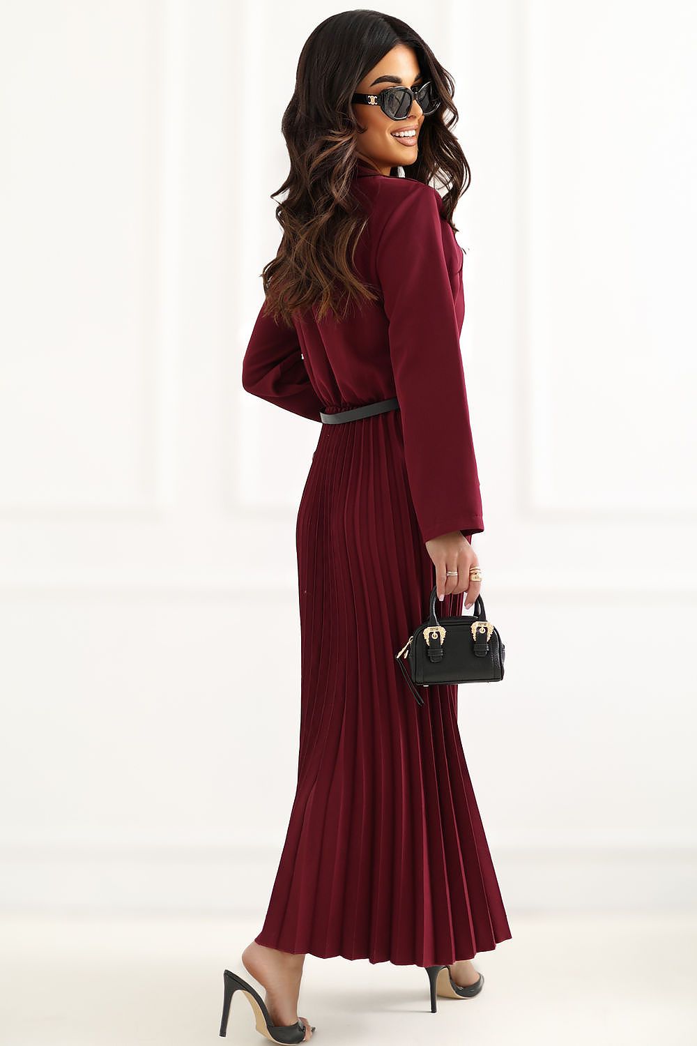 Woman wearing a burgundy dress holding a black handbag on a white background