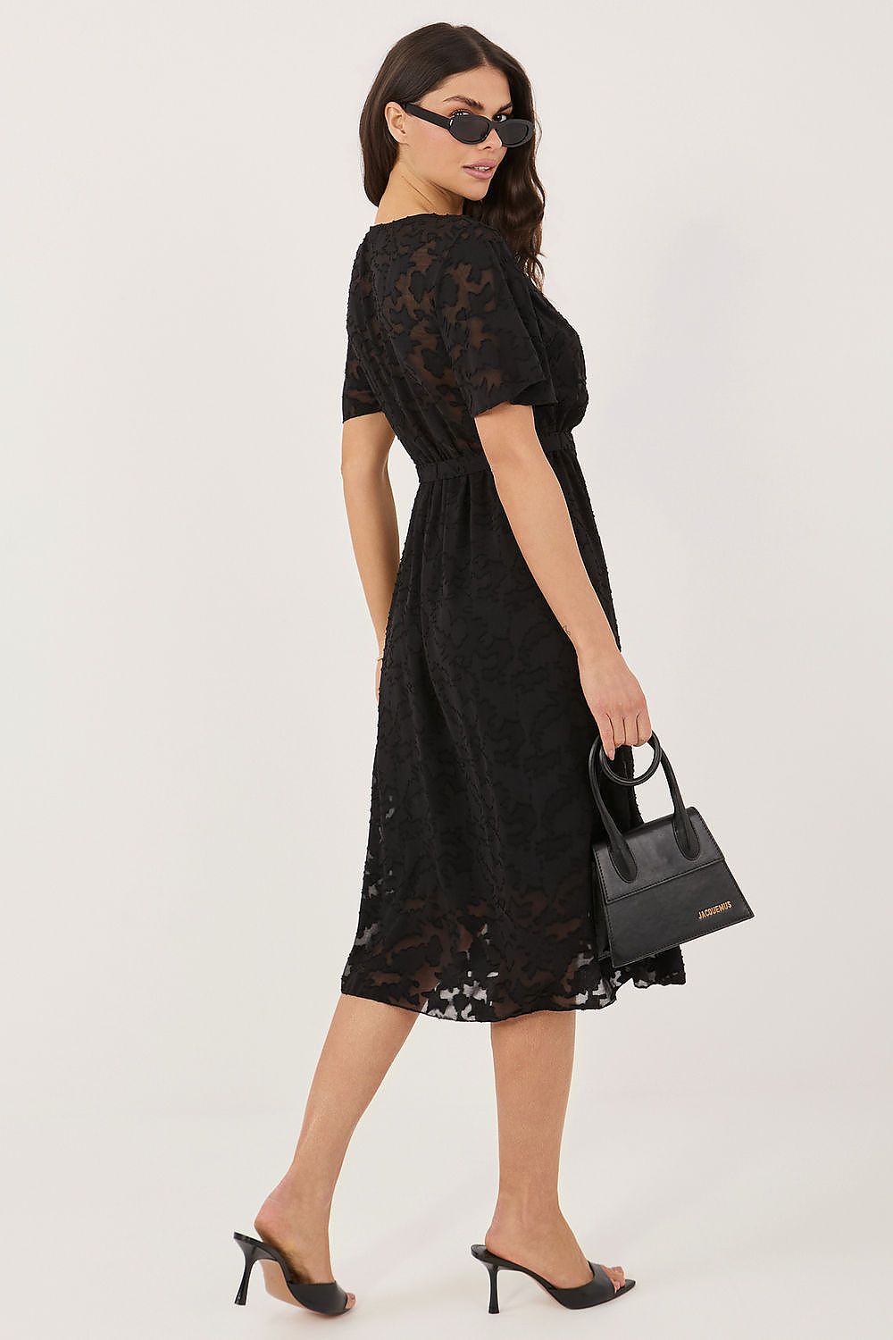 Woman wearing a black lace dress holding a matching handbag on a white background