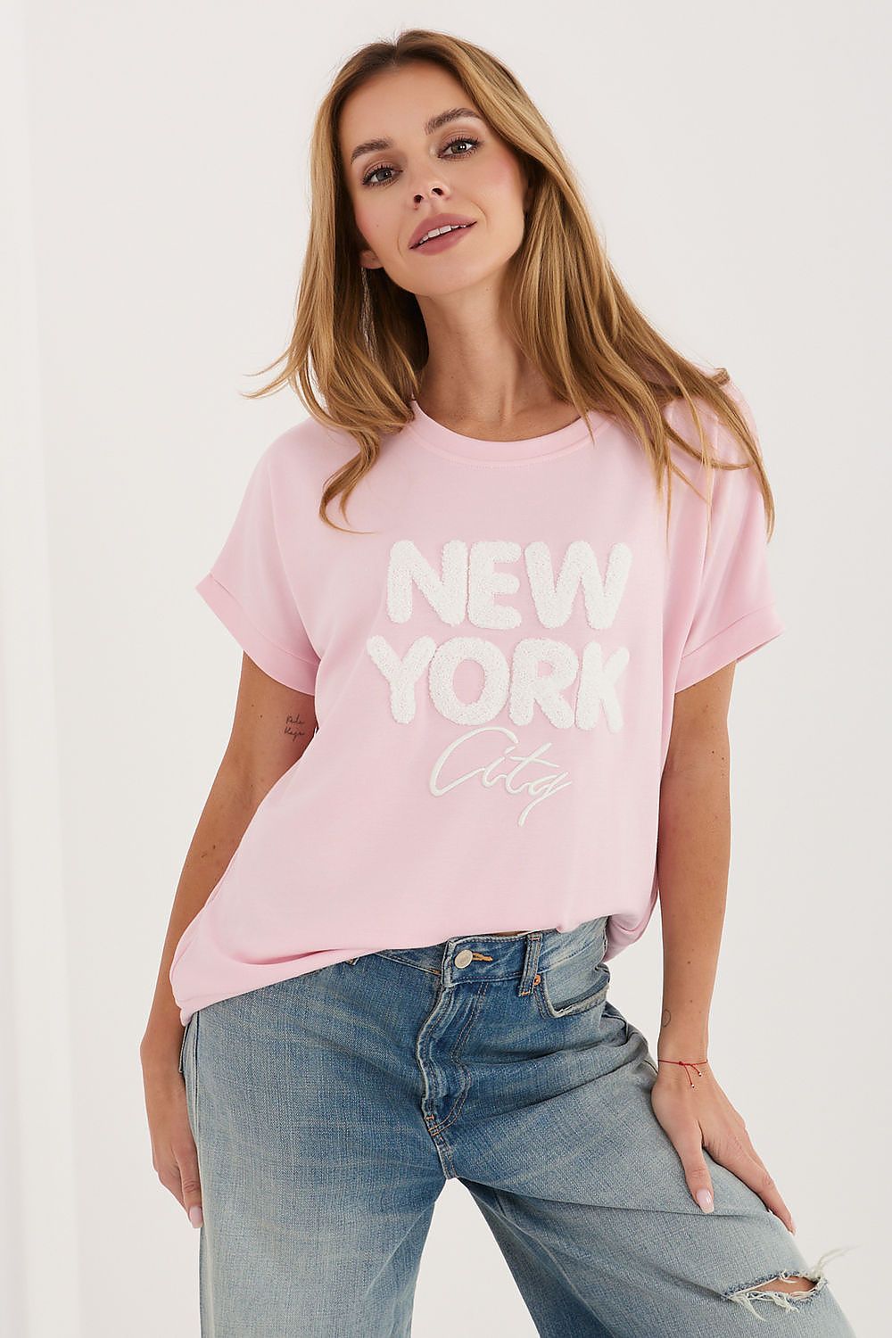 Woman wearing a pink 'New York City' t-shirt and blue jeans on a white background