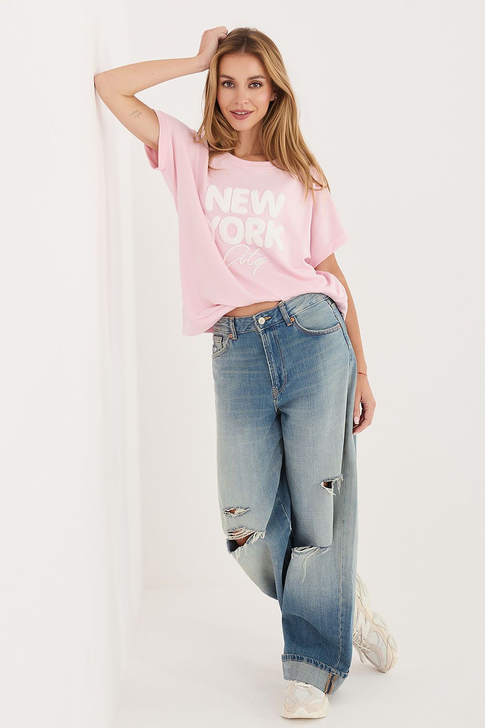 Woman wearing a pink 'New York' t-shirt and blue jeans on a white background