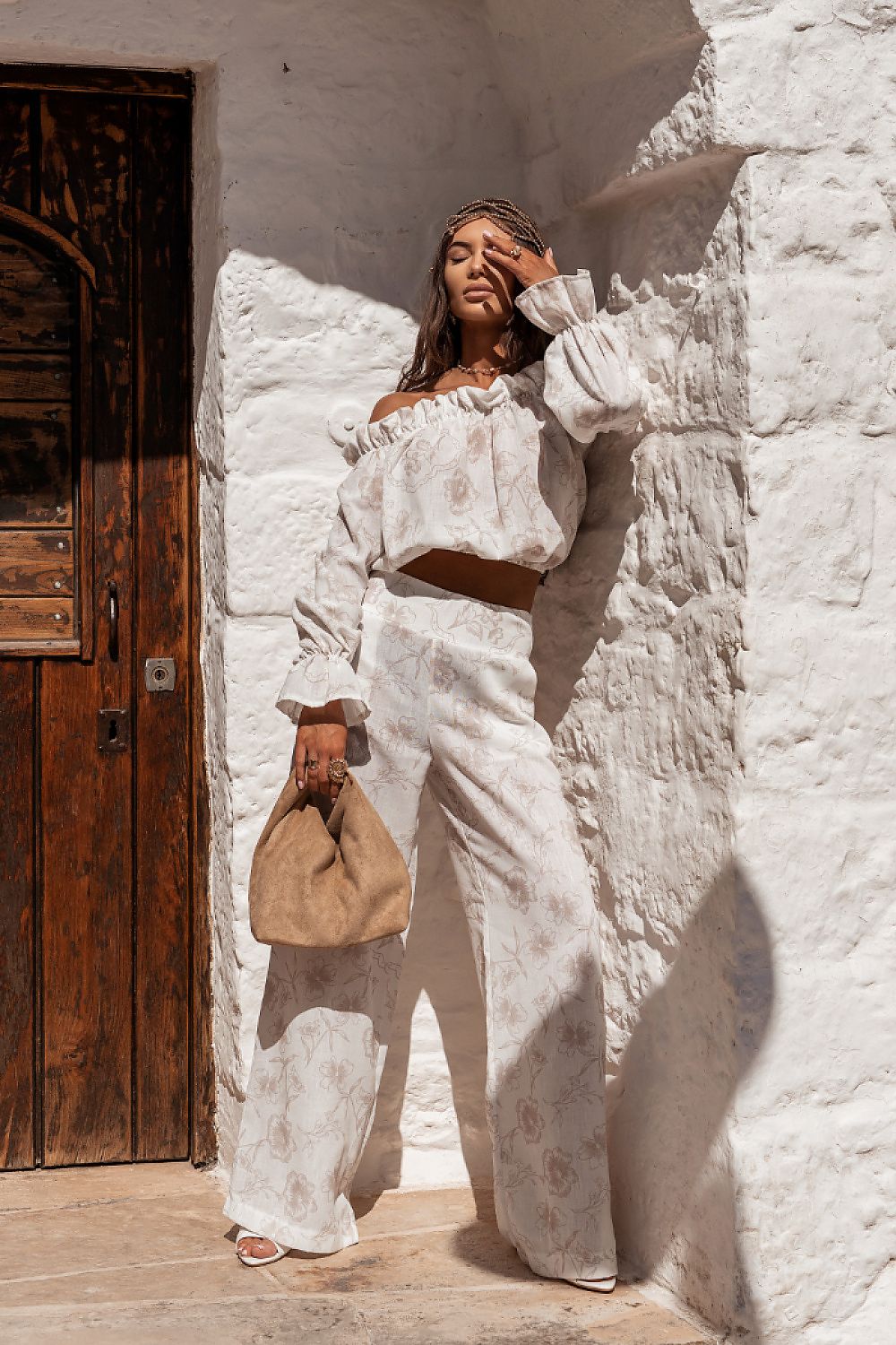 Woman in a white outfit standing against a textured white wall.