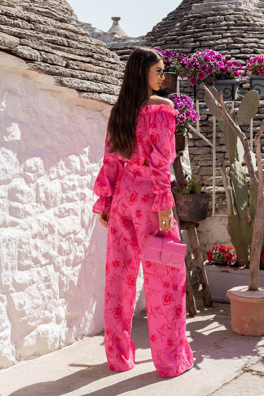 Woman in a pink floral outfit standing in front of traditional conical-roofed buildings.
