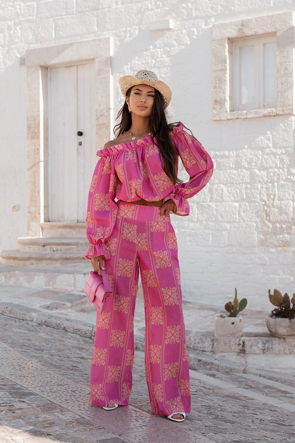 Woman in a pink patterned outfit standing in front of a white building.