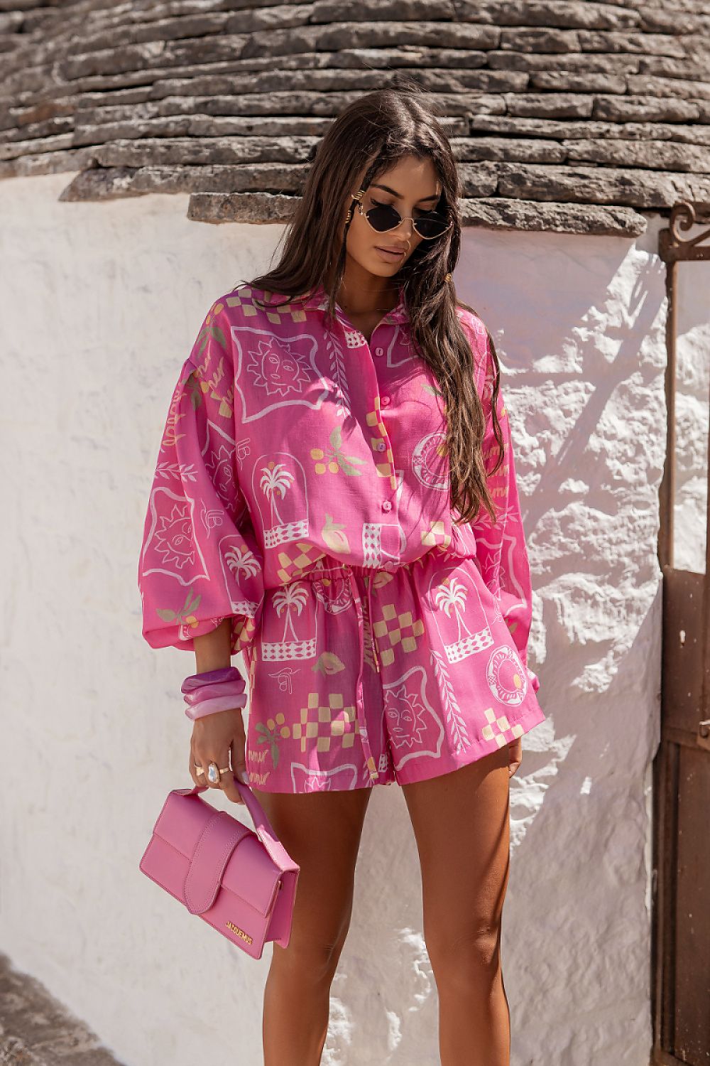 Woman wearing a pink outfit with palm tree patterns against a textured wall.